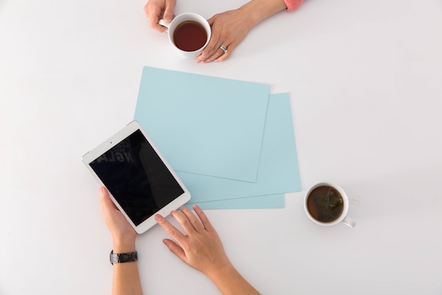 mesa branca com dois copos de café e folhas A4 azuis com funcionária segurando um tablet conversando com a sua cliente sobre as vantagens e o que é 4g